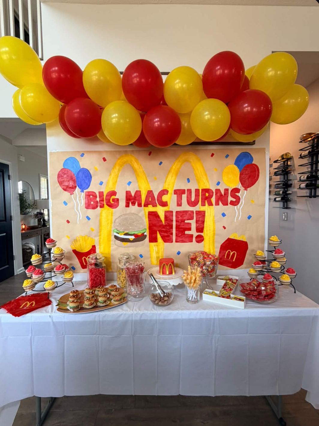 First birthday dessert table with red and yellow balloon garland and hand-painted backdrop