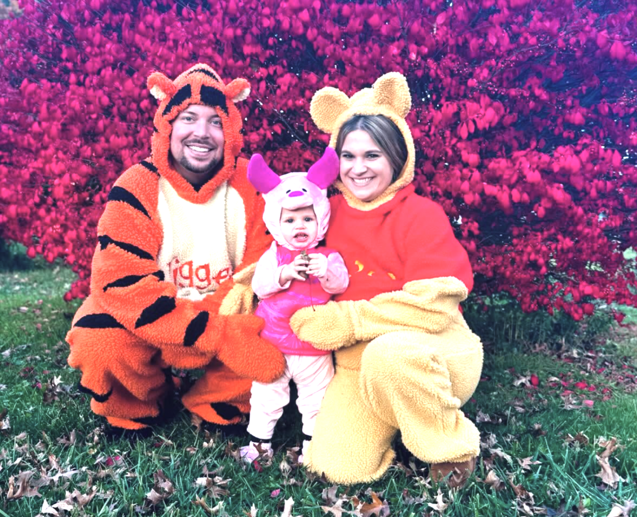 Family in Winnie the Pooh, Tigger and Piglet Halloween costumes in front of a crimson bush